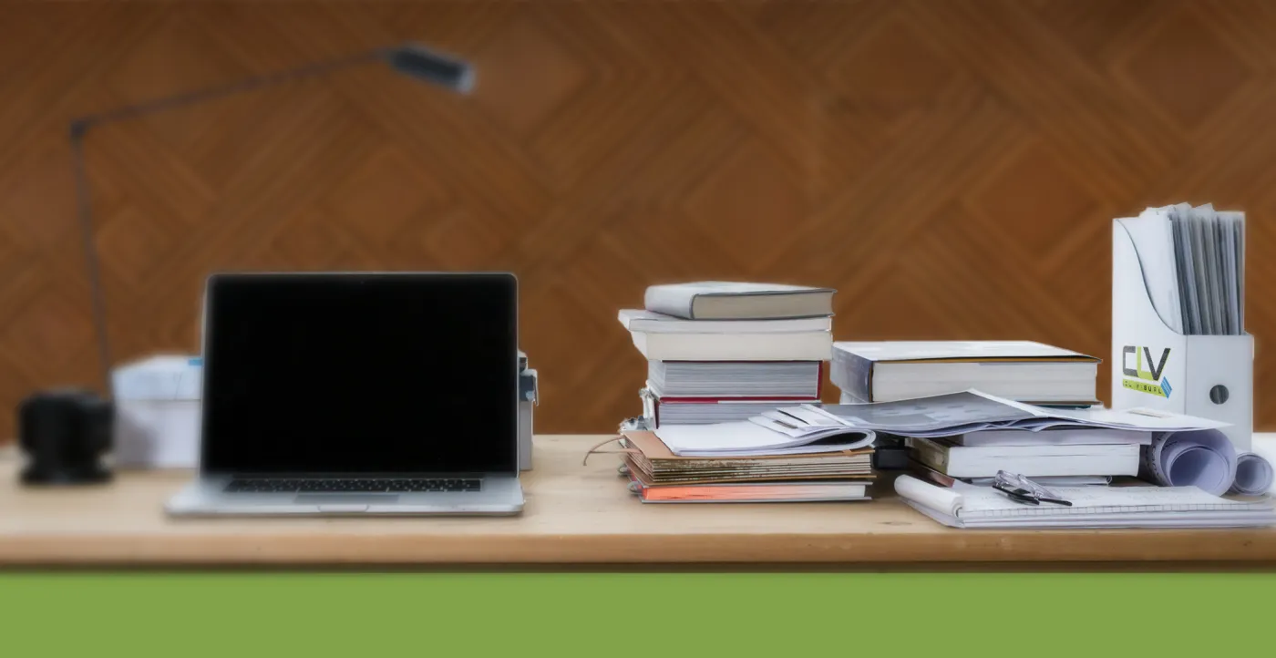 A desk with a laptop, stacked books and reference binders