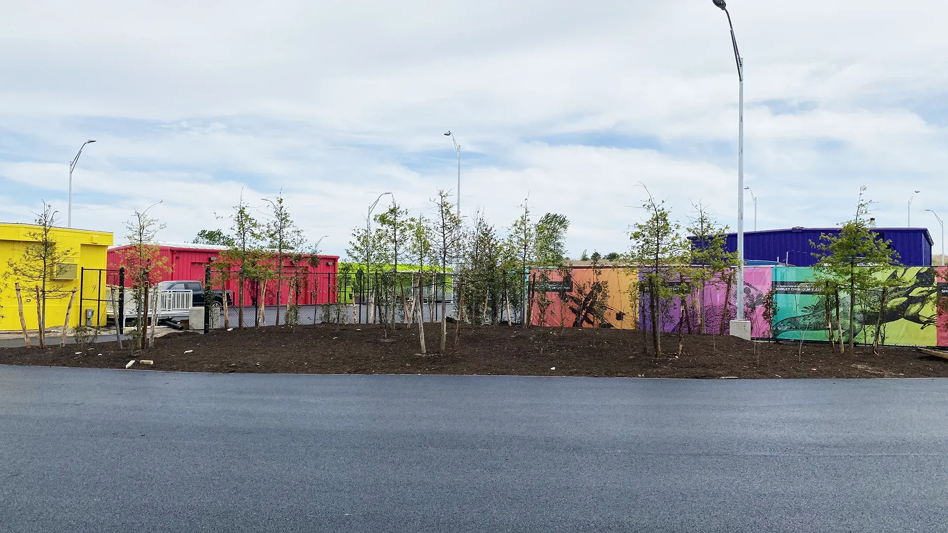 Row of colorful mesh fence banners along the parking area at Shirley Chisholm State Park