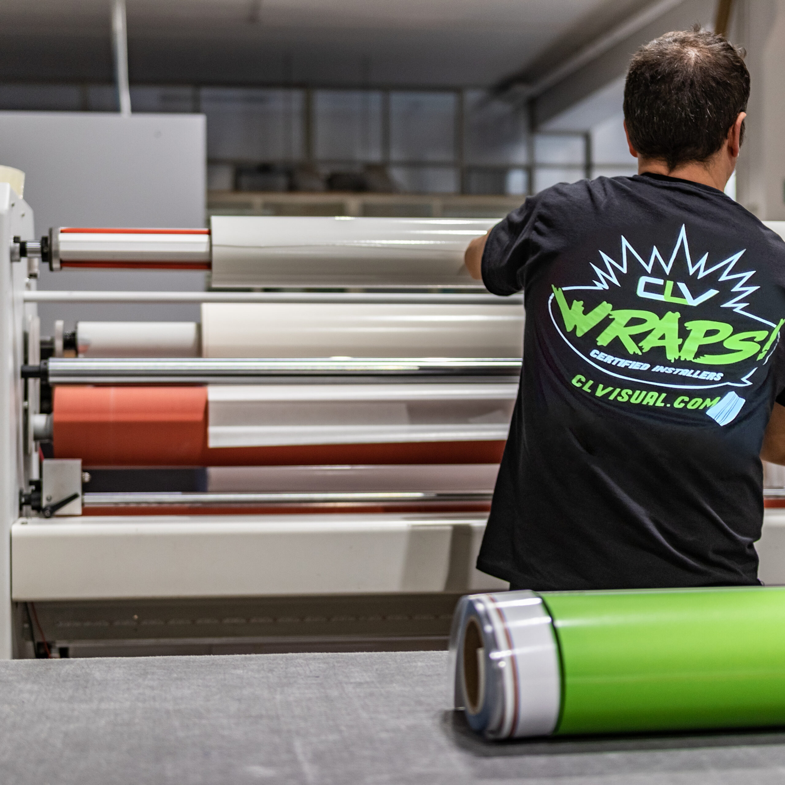 Specialized staff working big vinyl rolls on a professional printing machine and laminator. Details of the preparation and paper feed. White tubes, industrial workplace, occupation concept.